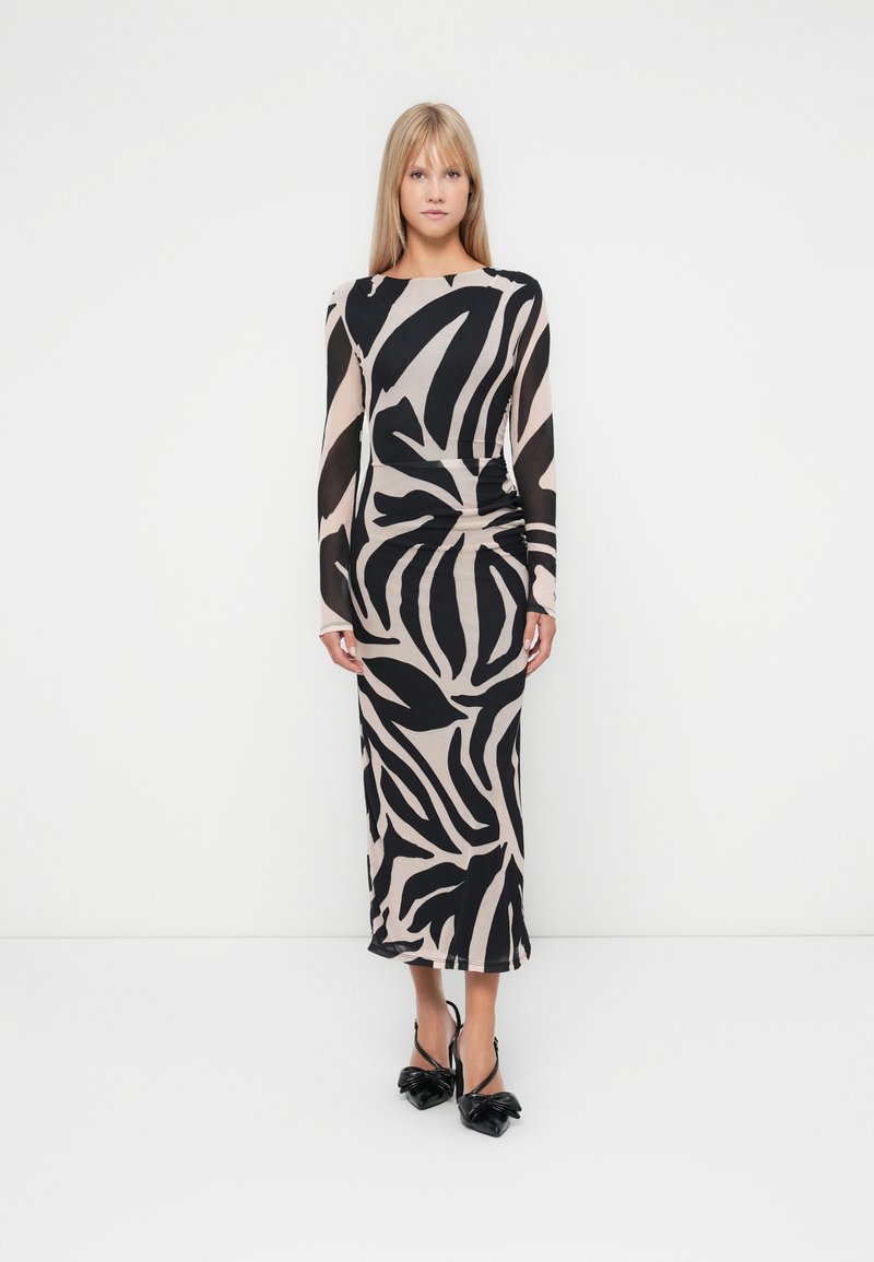 Robe à manches longues, longue jusqu'au sol, de couleur beige avec des motifs abstraits noirs. Tissu doux, design ajusté et silhouette élégante. Associée à des escarpins noirs.