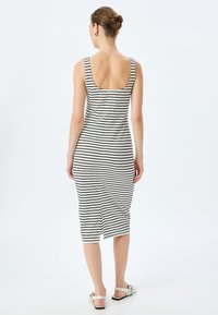 Gestreepte midi-jurk met een ronde rug, voorzien van zwart-witte strepen, aansluitend ontwerp en een zijsplit. Gemaakt om te dragen met witte sandalen.
