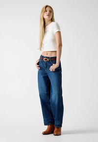 Donkere, wijde jeans met hoge taille, gecombineerd met een korte, witte, aansluitende T-shirt, afgewerkt met een bruine riem en bruine enkellaarzen.