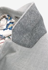 Giacca grigia con un colletto testurizzato di un grigio scuro. L'interno presenta un motivo floreale in tonalità blu e crema su uno sfondo chiaro.