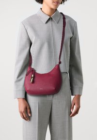 Borsa a tracolla in pelle borgogna con una texture liscia, forma curvata, chiusura con zip e un accento in hardware dorato.