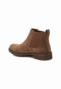 Botines de ante marrón con paneles laterales elásticos, puntera curvada y suela de goma texturizada. Presenta un tirador en el talón reforzado para facilitar su uso.