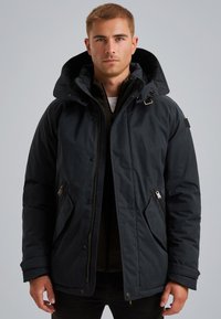 Črna izolirana jakna z veliko kapuco, zadrženimi žepi in gladko, rahlo sijočo površino. Dodatki vključujejo srebrno kovinsko opremo.