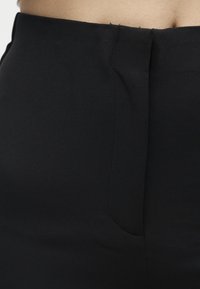 Κοντινή λήψη μαύρης ζώνης φούστας με κρυφό πλαϊνό φερμουάρ πάνω σε γυμνό δέρμα.