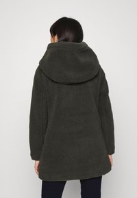 Abrigo de forro polar verde oscuro con una capucha grande y suave, mangas largas y un ajuste relajado. La textura es suave y acogedora, con un acabado liso.