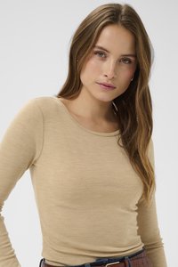 Hosszú ujjú, bézs színű, puha, texturált anyagból készült felső kerek nyakkivágással, barna övvel párosítva. Egyszerű és testhezálló fazon.