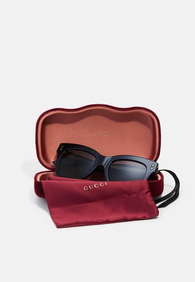 Melnas lielas saules brilles ar tumšiem objektīviem burgundijas samtā. Iekšpuse ir gluda ar zelta "GUCCI" zīmolu. Ietver atbilstošu maisiņu.