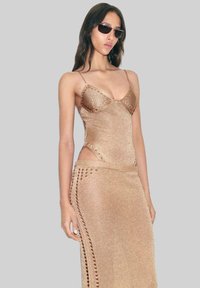 Knit two-piece outfit in a shimmery gold tone. Features spaghetti straps, side cutouts, and decorative stitching along the waistband.