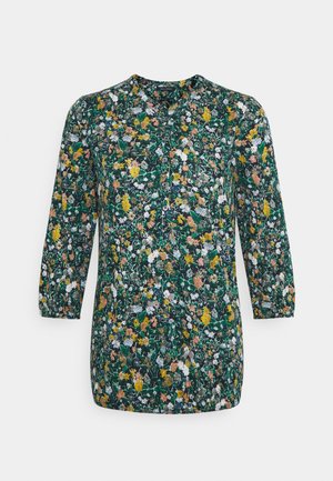 Blouse florale avec des manches trois-quarts, présentant un fond vert foncé et un motif de fleurs jaunes, roses et blanches. Encolure ronde.