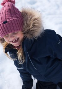 Marineblå parka med pelsbesat hætte, grå accenter og sort label; pink strikket hue med pompon; barn der leger i sneen.