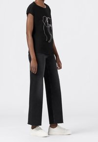 Svart kortärmad t-shirt med vit elefantkonturdesign, kombinerad med högmidjade svarta vida jeans och vita sneakers.