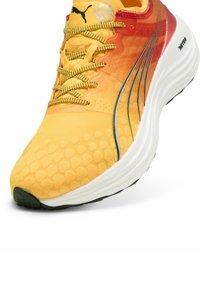 Zapatilla de correr Puma con un diseño en degradado de amarillo a rojo, textura hexagonal, cordones en un brillante amarillo y una suela robusta blanca con acentos negros.