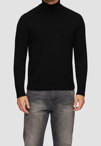 Czarny sweter z golfem, wykonany z miękkiej dzianiny, z długimi rękawami i prążkowanymi mankietami, w połączeniu z jasnoszarymi dżinsami o wyblakłej fakturze.