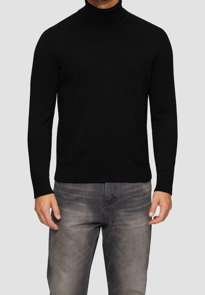 Czarny sweter z golfem, wykonany z miękkiej dzianiny, z długimi rękawami i prążkowanymi mankietami, w połączeniu z jasnoszarymi dżinsami o wyblakłej fakturze.