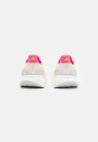 Une paire de chaussures de sport blanches avec des talons roses, des bandes jaunes fluo et des semelles blanches texturées, vues de l'arrière sur un fond blanc.