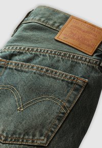 Jean Levi's en denim bleu plié pour montrer la poche arrière avec des coutures jaunes et une étiquette en cuir marron Levi Strauss & Co.