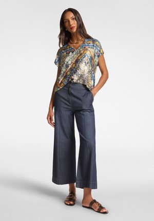 Top multicolore con motivo, caratterizzato da una scollatura a V e maniche corte, abbinato a pantaloni di jeans ampi neri e sandali pianeggianti marroni.