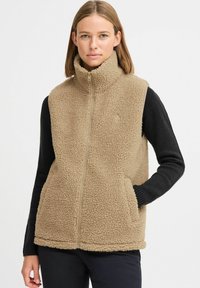Gilet en polaire beige avec un col montant, une fermeture éclair à l'avant et des poches latérales. Présente des manches longues noires et un tissu texturé.