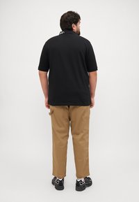 Μαύρο κοντομάνικο πόλο μπλουζάκι με ριχτό γιακά, συνδυασμένο με μπεζ cargo παντελόνι με πλαϊνές τσέπες, και μαύρα αθλητικά παπούτσια με λευκές λεπτομέρειες.