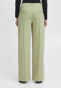 Svetlozeleni široki hlače s prilagojenim krojem, z zadnjimi žepki in mehkim tekstilom. Čist dizajn brez vidnih vzorcev.