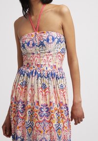 Robe sans bretelles avec un lien autour du cou, ornée d'un motif floral et géométrique coloré en bleu, rose, orange et jaune sur un tissu blanc.