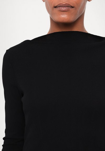 Sort ribbet langærmet top med høj halsudskæring. Stoffet ser glat ud med en tætsiddende design, der har teksturerede lodrette linjer.