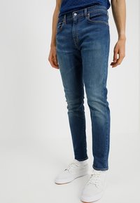 Smal passform blå jeans i denim, med en urtvättad finish, femficksdesign och subtil sömnad. Matchas med vita sneakers.