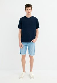Camiseta de manga corta de rayas en color navy combinada con pantalones cortos de mezclilla azul claro y zapatillas blancas con detalles en marrón. Diseño sencillo y casual.