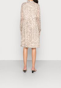 Šaty s květinovým vzorem, průhledné, v béžové barvě, s dlouhými rukávy a nařaseným pasem, doplněné o sandály na průhledném podpatku. Viditelný detail texturované látky.