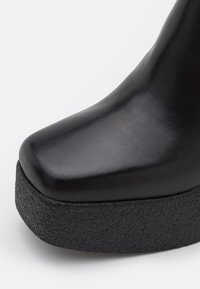 Chaussure à plateforme en cuir lisse noir avec une semelle épaisse et texturée, montrant les détails avant et latéraux.