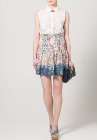 Vestido floral con una parte superior sin mangas blanca, falda con colores degradados de rosa a azul, diseño pliegues, combinado con un bolso azul y tacones grises.