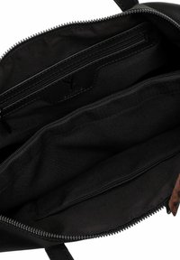 Interno di una borsa a mano in pelle nera con più scomparti; presenta una tasca con zip, una consistenza liscia e cuciture resistenti.