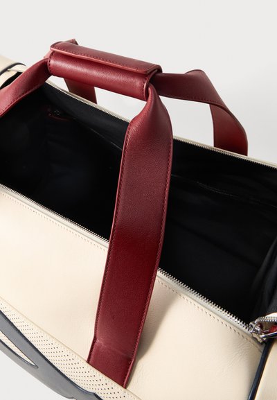 Μπεζ και μαύρη δερμάτινη τσάντα με φαρδιές μπουρντό λουράκια και ανοιχτό φερμουάρ που δείχνει το μαύρο εσωτερικό φόδρας.