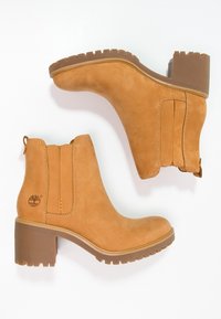 Marron suede nilkkurit, joissa on pinoettu korko, joustavat sivupaneelit ja vetotappi; brändin motiivi ja teksturoitu kumipohja.