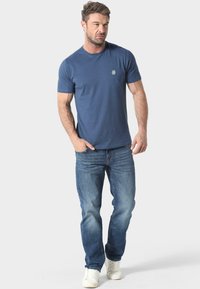 Camiseta de algodón azul marino para hombre, de manga corta y cuello redondo, con un pequeño logo bordado en el pecho, combinada con jeans azules y zapatillas blancas.