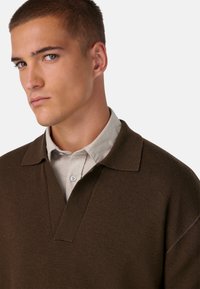 Pruunist kudumist polo-särgist, millel on V-kaelus ja lühike krae, mis katab heledat halli nööpidega särke. Omab sujuvat tekstuuri ja klassikalist lõiget.