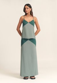 Grøn lagdelt kjole med halterneck, med geometriske farveblokke i nuancer af grøn og et gulvlængde, flydende design.