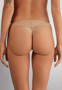 Lace string in nude, met een delicaat bloemenpatroon, elastische tailleband en een lage taille, die minimale bedekking aan de achterkant biedt.