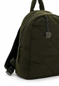 Mochila acolchada de color verde olivo con un exterior texturizado y cremallera de metal. Cuenta con un panel trasero de malla y un colgante de logo en cadena.