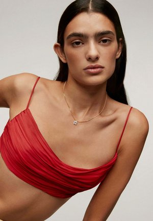 Top corto rojo con fruncidos y tirantes finos, combinado con un delicado collar de oro que cuenta con un pequeño colgante transparente. Textura de tela suave.