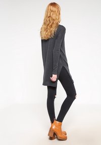 Maglione a maniche lunghe grigio scuro con spacchi laterali, indossato sopra jeans skinny neri strappati. Abbinato a stivaletti marroni con tacco.