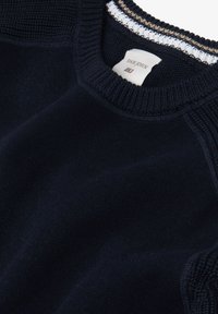 Navy sininen neulosneule, jossa on tekstuurinen pyöreä kaula-aukko ja kontrastiväriset valkoiset ja beige-väriset raidat kauluksessa ja hartioilla.