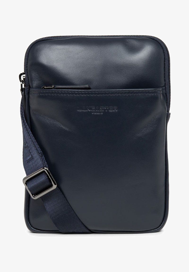 Sac bandoulière en cuir bleu marine avec fermeture éclair, doté d'une poche avant et d'une sangle ajustable. Texture lisse avec détail de logo en relief.