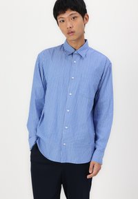 Blue striped button-up shirt with a collar, long sleeves, and a chest pocket; features vertical white stripes and a relaxed fit.