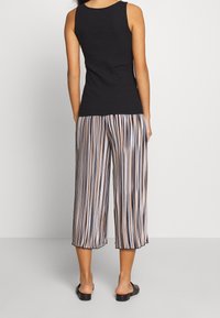 Top a coste nero abbinato a pantaloni larghi con righe verticali in blu navy, beige e crema. Tessuto liscio e lunghezza cropped.