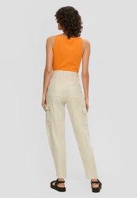 Oranje geribde tanktop gecombineerd met lichtbeige cargo pants met voorzakken. Model draagt zwarte platform sandalen.