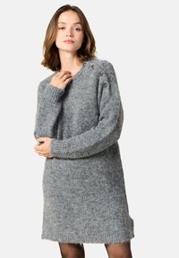 Grå stickad klänning med lång ärm, rund halsringning, textilstruktur och dekorativa knappar på axeln. Mjuk, lös passform.