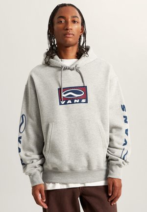 Felpa grigia con cappuccio e tasca frontale, con un logo grafico in blu e rosso. Le maniche lunghe presentano la scritta "VANS" in blu. Design casual.