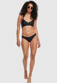 Črn bikini z nastavitvenim vrhom v obliki trikotnika, ki je združen z minimalizmom bikinija, ki izhaja iz gladkih tkanin in preprostih linij.