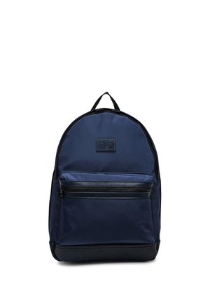 Tmavě modrý batoh s přední kapsou na zip, černým dnem, horním úchopem a značkovou nášivkou s nápisem "G-STAR ORIGINALS RAW" na přední straně.